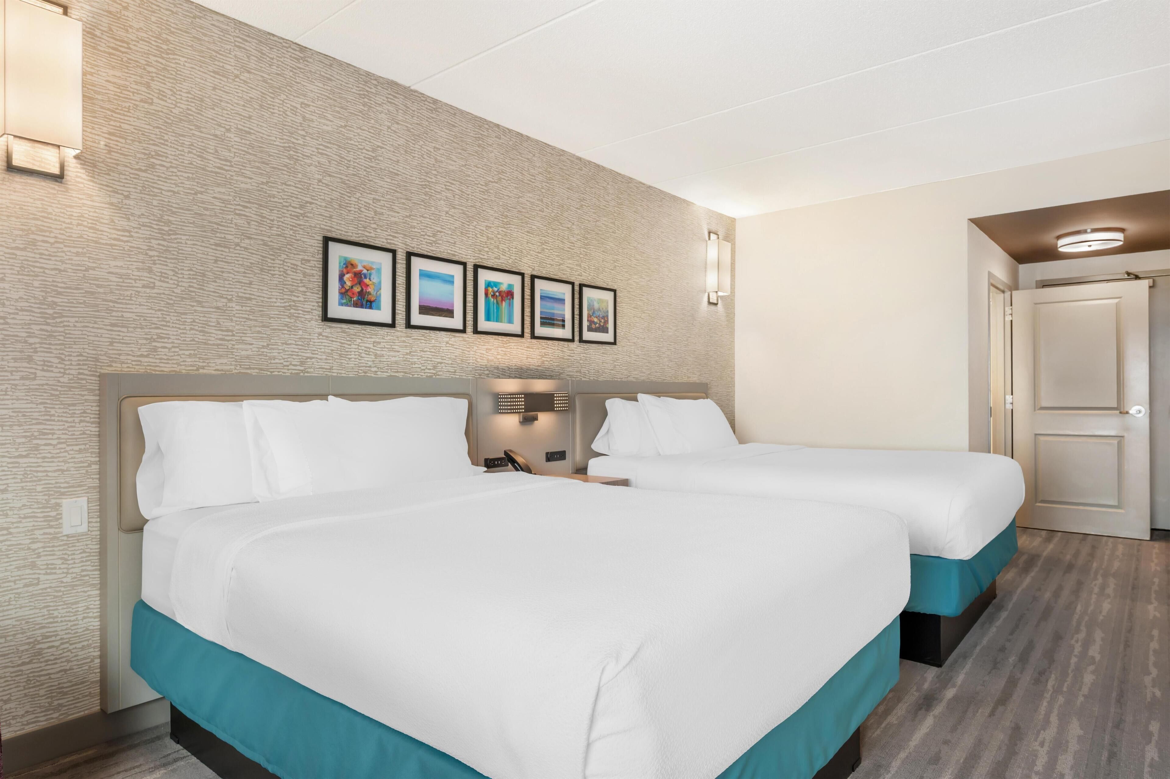A hotel room with two beds, a brick-patterned wall, and framed artwork above the beds.