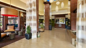 A spacious lobby with a high ceiling, brick columns, and a mix of seating areas including sofas and chairs. - Hilton Garden Inn Wisconsin Dells (Wisconsin Dells)