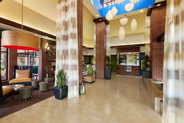 A spacious lobby with a high ceiling, brick columns, and a mix of seating areas including sofas and chairs.