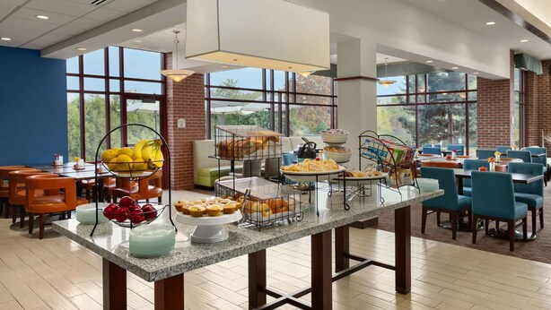 A spacious dining area with a buffet table, large windows, and a brick wall. - Hilton Garden Inn Wisconsin Dells (Wisconsin Dells)