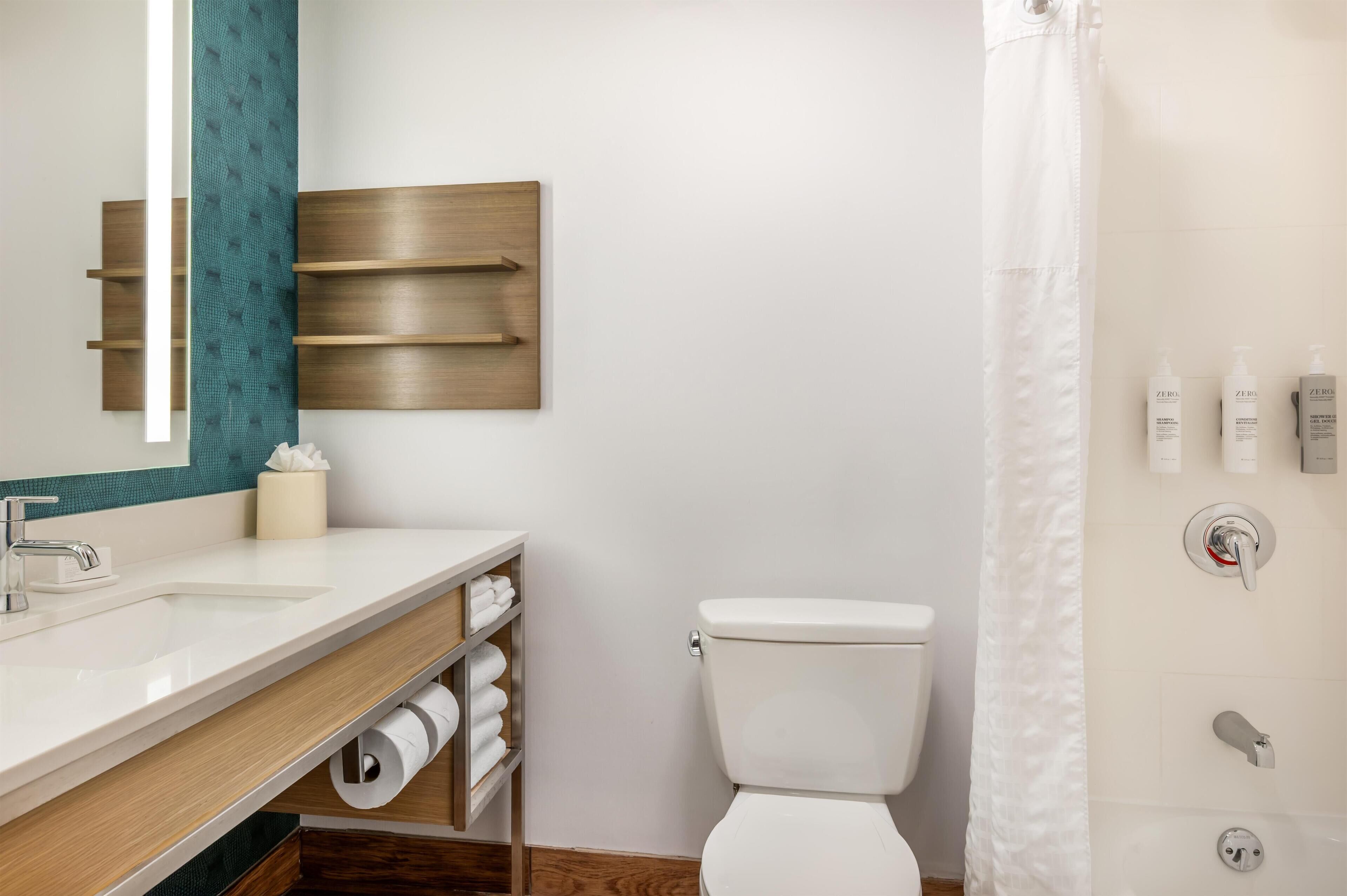 Un baño moderno con un lavamanos blanco, un espejo, un inodoro y una cortina de ducha.