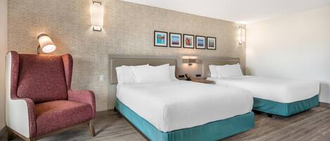 A hotel room with two beds, a red armchair, and wall-mounted artwork.