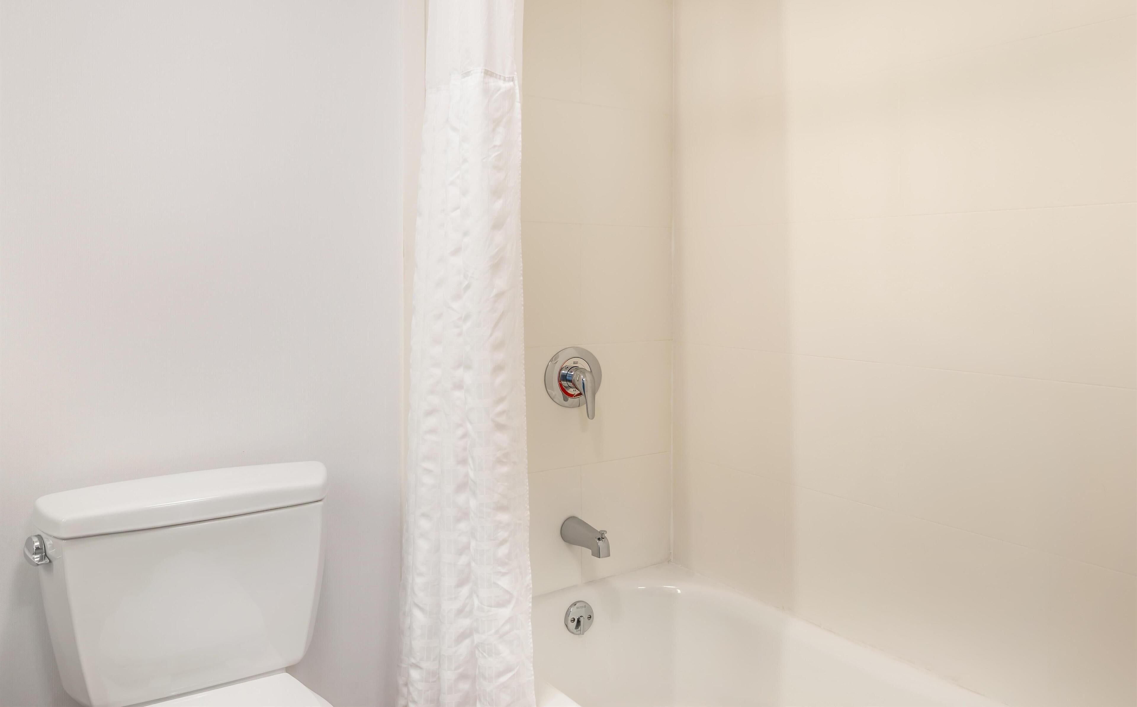 A bathroom with a toilet, a shower with a curtain, and a bathtub.