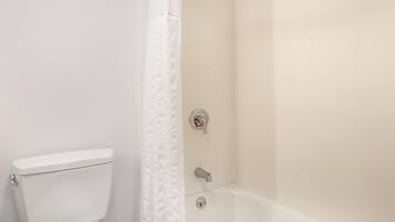 A bathroom with a toilet, a shower with a curtain, and a bathtub.
