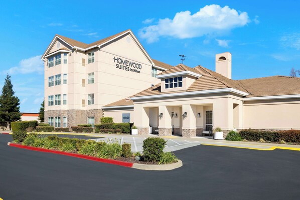 A hotel with a beige exterior, a large parking lot, and a clear blue sky. - Homewood Suites by Hilton Sacramento Roseville (Roseville)