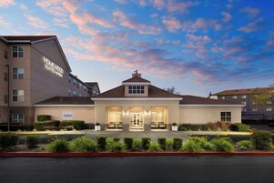 Un hotel dal design moderno, con un ingresso imponente e una tettoia, un paesaggio curato e una vista aperta sul cielo.