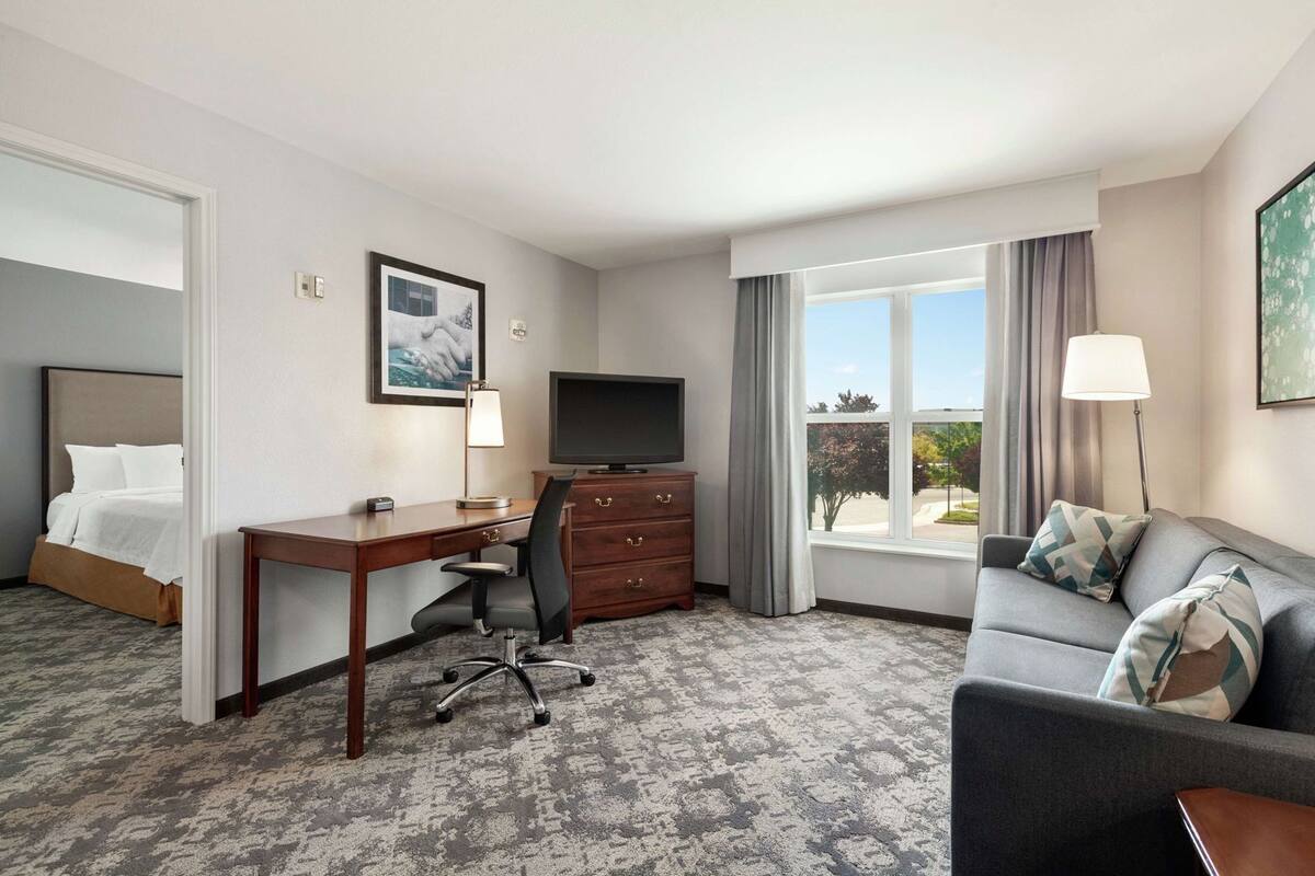 Una habitación de hotel con cama, escritorio, silla, televisor, cómoda y sofá.