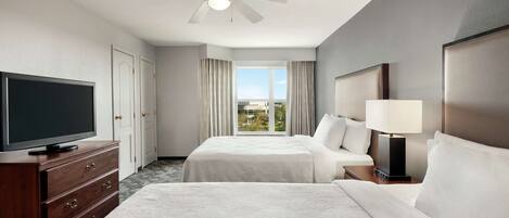 A hotel room with two beds, a TV, a ceiling fan, and a view of the outdoors.