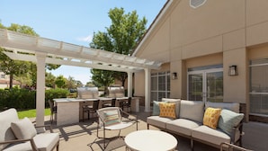 Un patio exterior con pérgola, mobiliario, una parrilla y vistas del paisaje circundante.