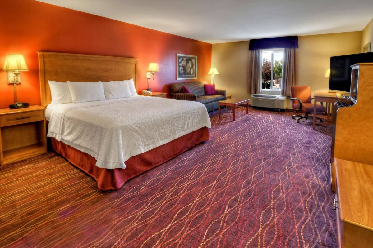 A hotel room with a large bed, a sofa, a desk, and a TV.