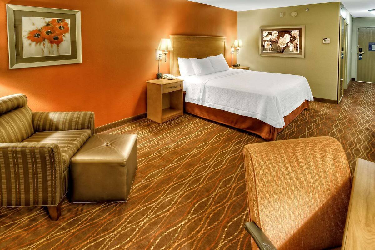 A hotel room with a large bed, two bedside tables with lamps, a sofa, and an ottoman.