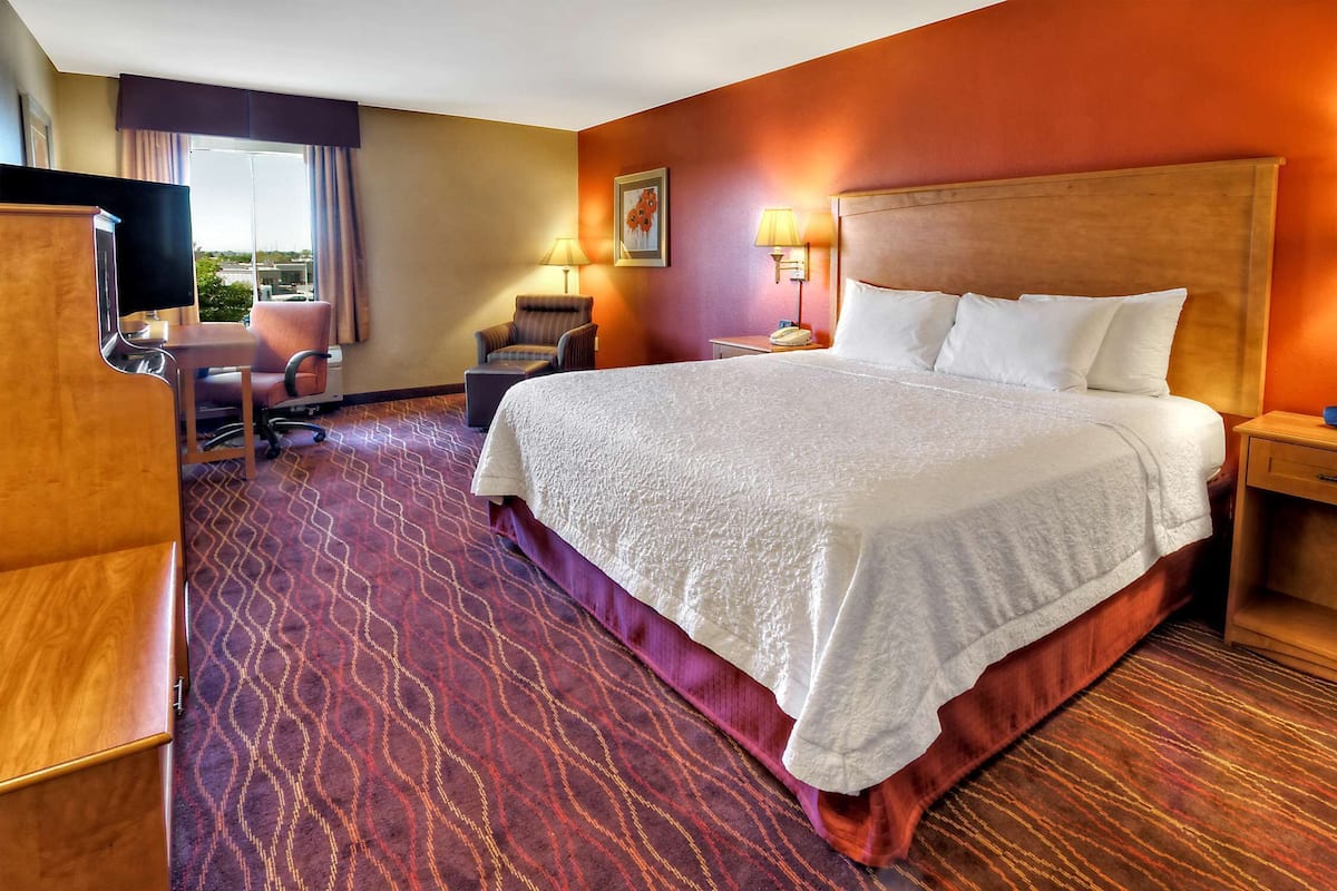 A hotel room with a large bed, a desk with a chair, a TV, and a window with curtains.