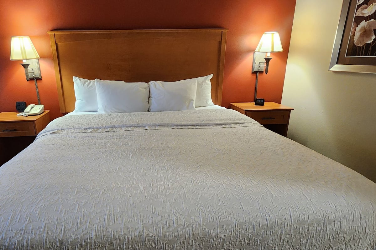 A hotel room with a large bed, two bedside lamps, a nightstand with a phone, and a framed picture on the wall.