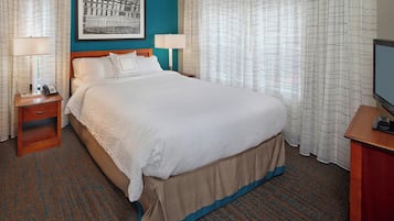 A hotel room with a large bed, two bedside tables with lamps, a flat-screen TV, and a framed picture on the wall.