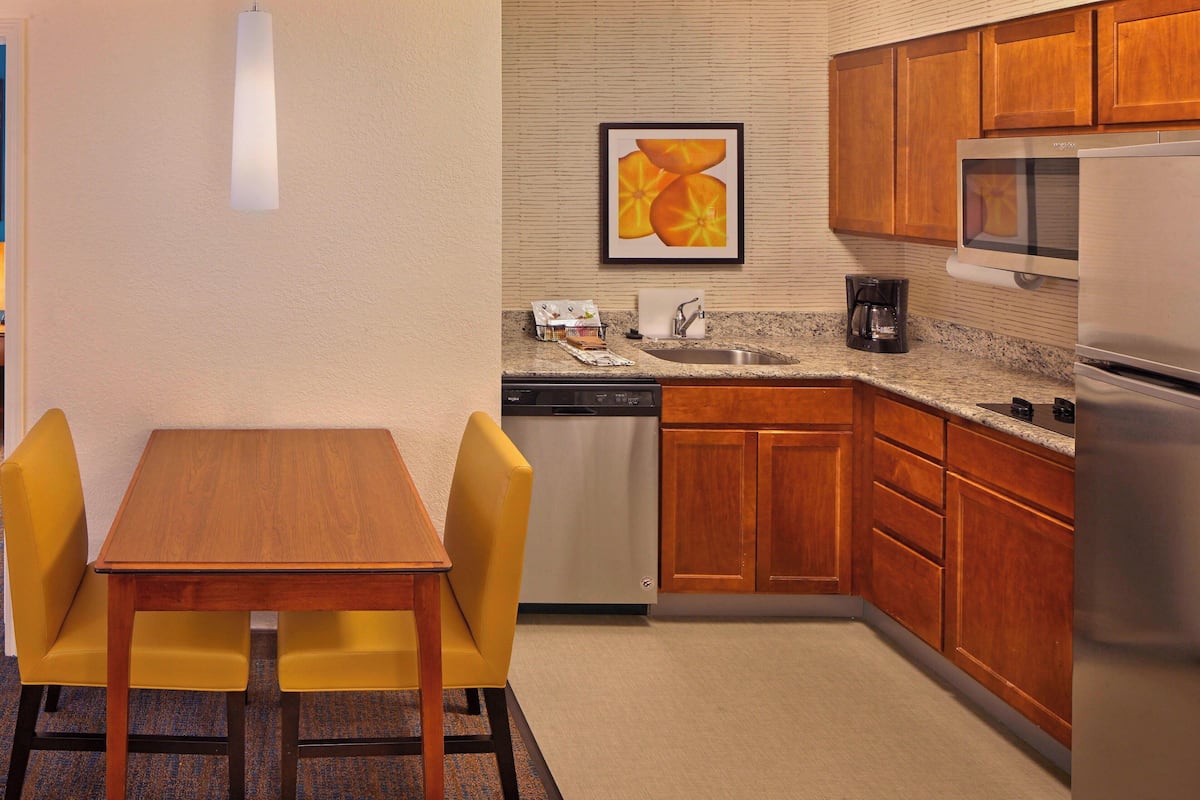 A compact kitchen with wooden cabinets, a microwave, a dishwasher, and a dining area with a table and two chairs.