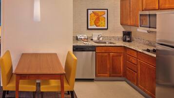 A compact kitchen with wooden cabinets, a microwave, a dishwasher, and a dining area with a table and two chairs.