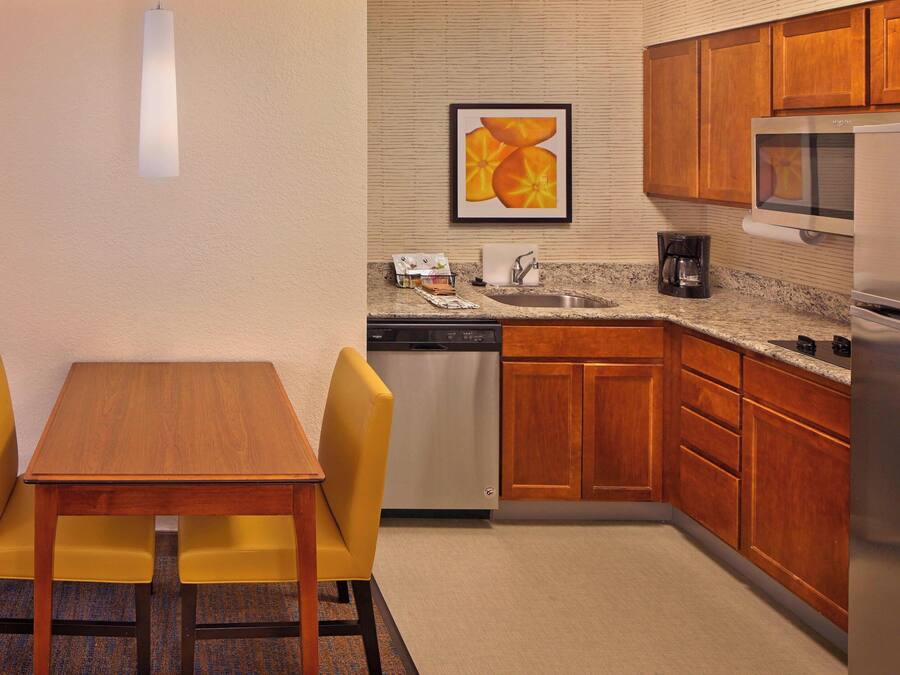 A compact kitchen with wooden cabinets, a microwave, a dishwasher, and a dining area with a table and two chairs.