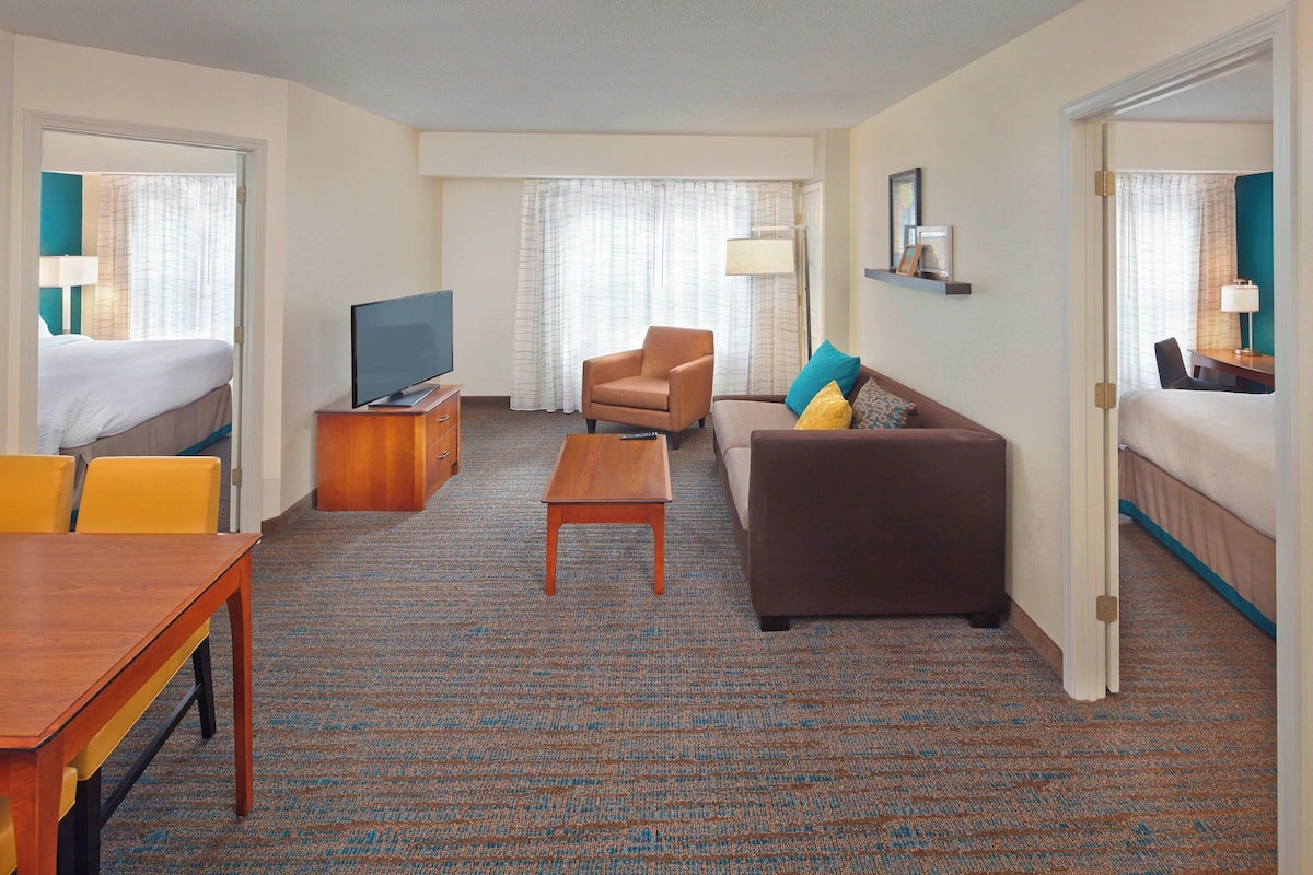 A hotel room with a bed, a sofa, a TV, a coffee table, and a desk.