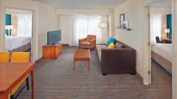 Una habitación de hotel con cama, sofá, televisión, mesa de centro y escritorio.