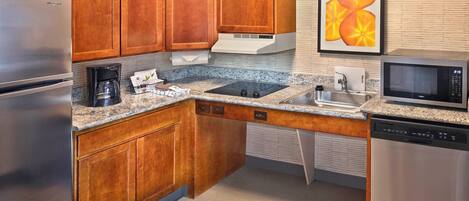 A compact kitchen with wooden cabinets, a stainless steel refrigerator, a microwave, and a dishwasher.