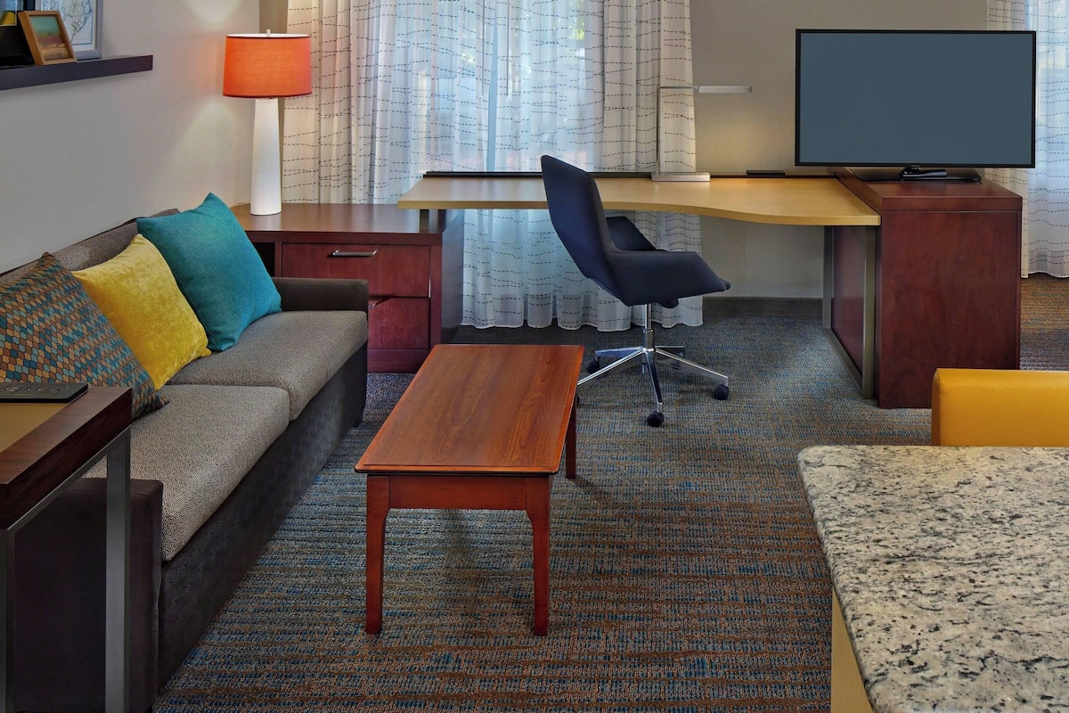 A hotel room with a sofa, a desk, a television, and a small table.