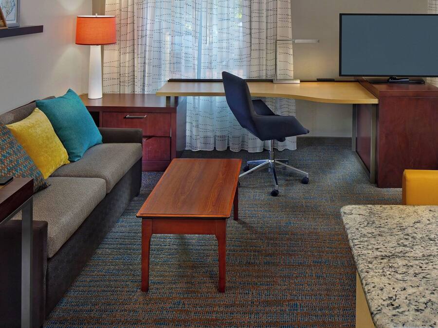 A hotel room with a sofa, a desk, a television, and a small table.