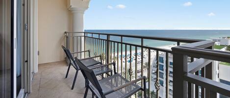 Un balcon avec deux chaises et une table, donnant sur une plage et un parking.