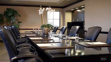 A conference room with a long table, black leather chairs, a plant, and a window.