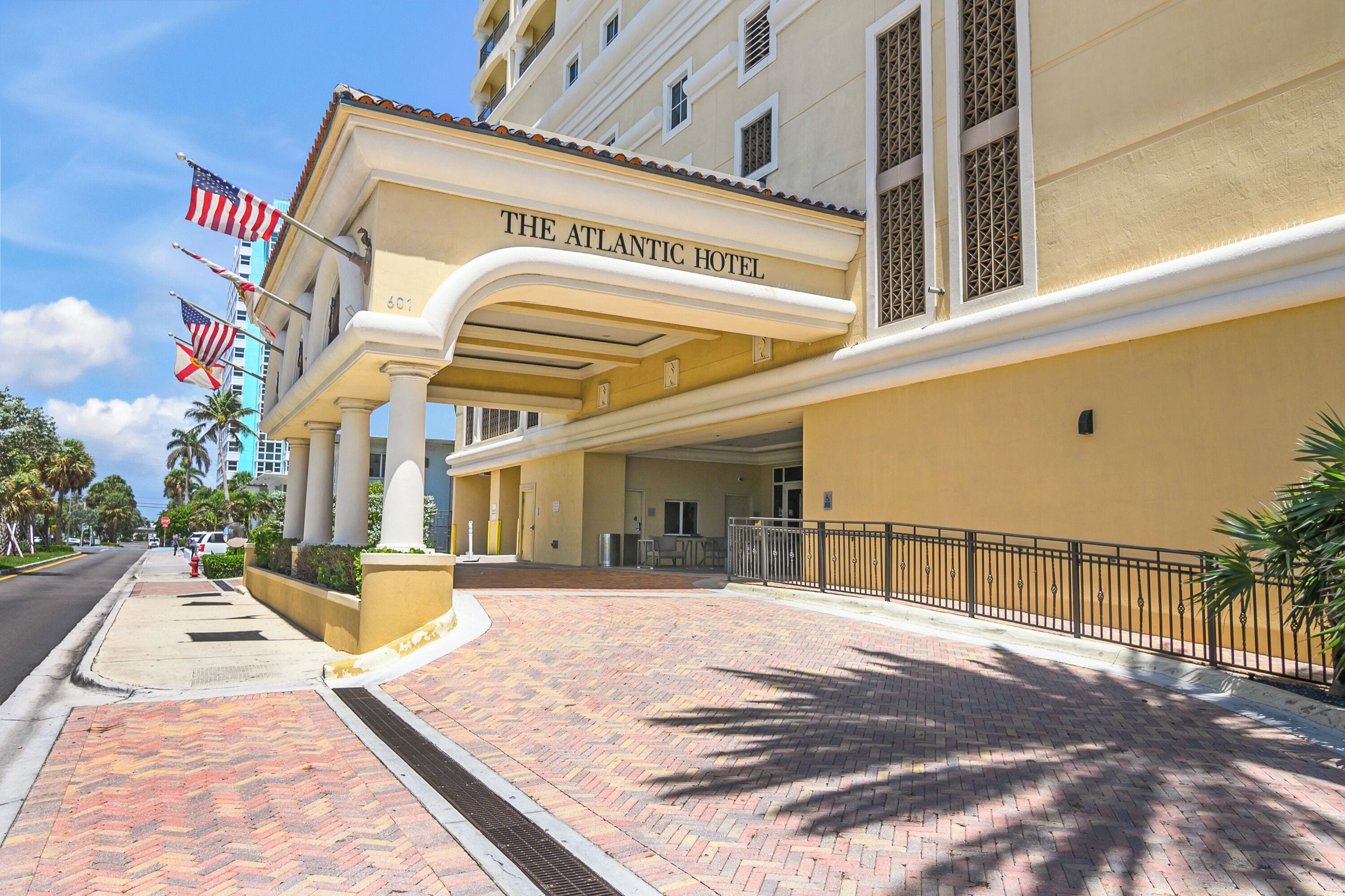 The Atlantic Hotel with a brick-paved entrance, palm trees, and American flags.