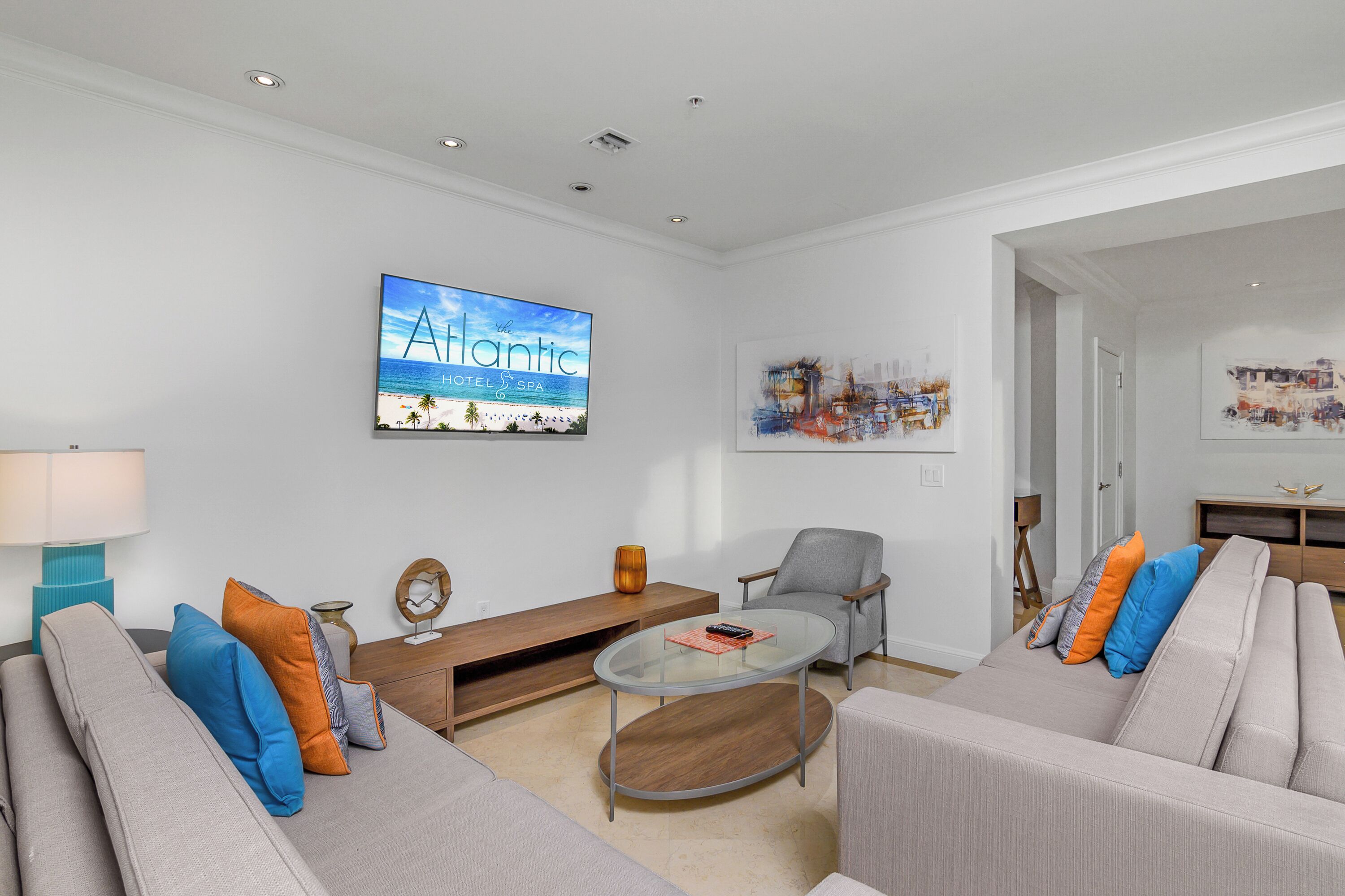 A modern living room with a sofa, armchairs, a coffee table, and a TV displaying 'The Atlantic Hotel & Spa'.