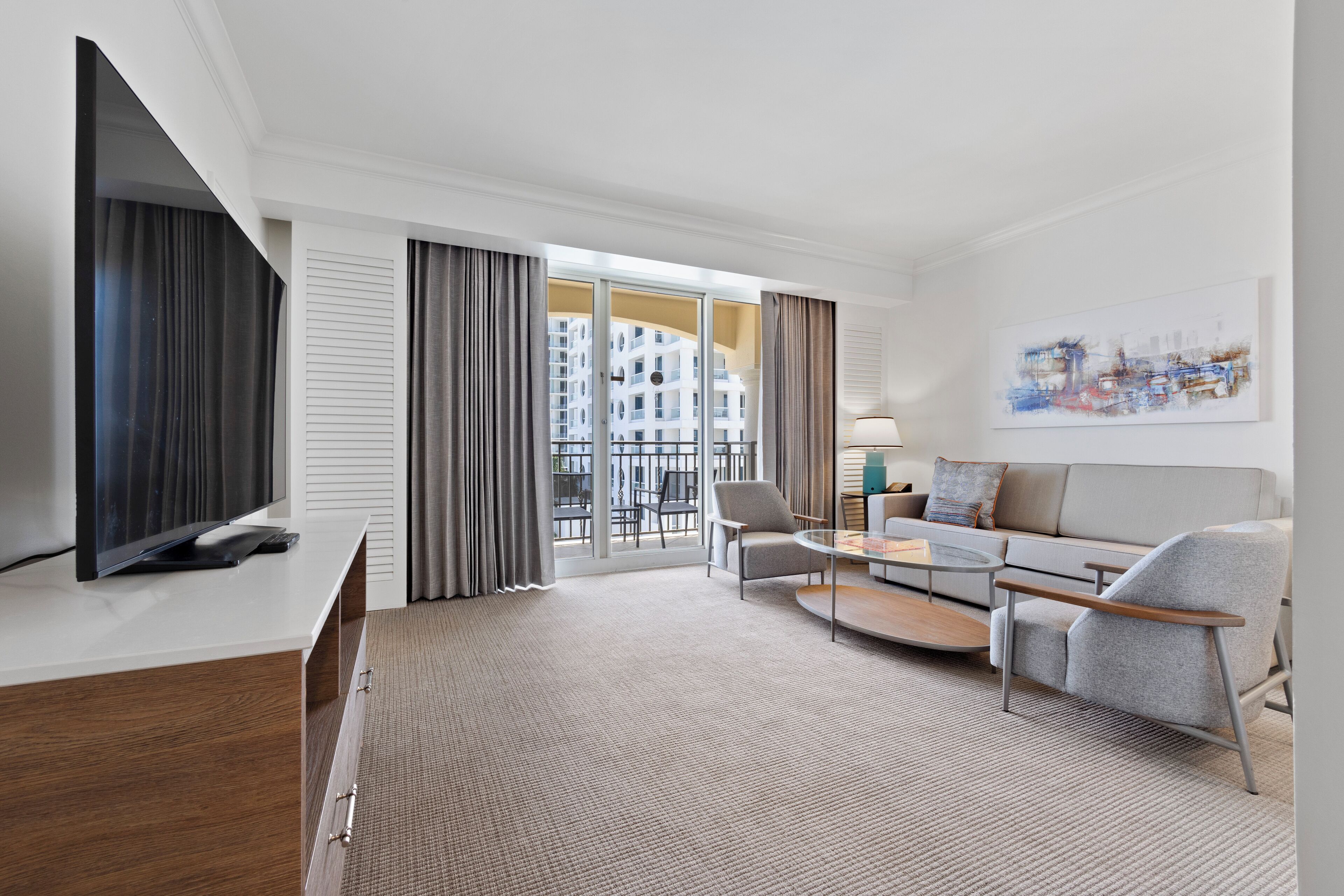 Een moderne hotelkamer met een flatscreen televisie, een bank, een bijzettafeltje en een balkon met uitzicht op gebouwen.