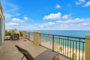 A balcony with a view of the sea, a table, chairs, and a small outdoor seating area.