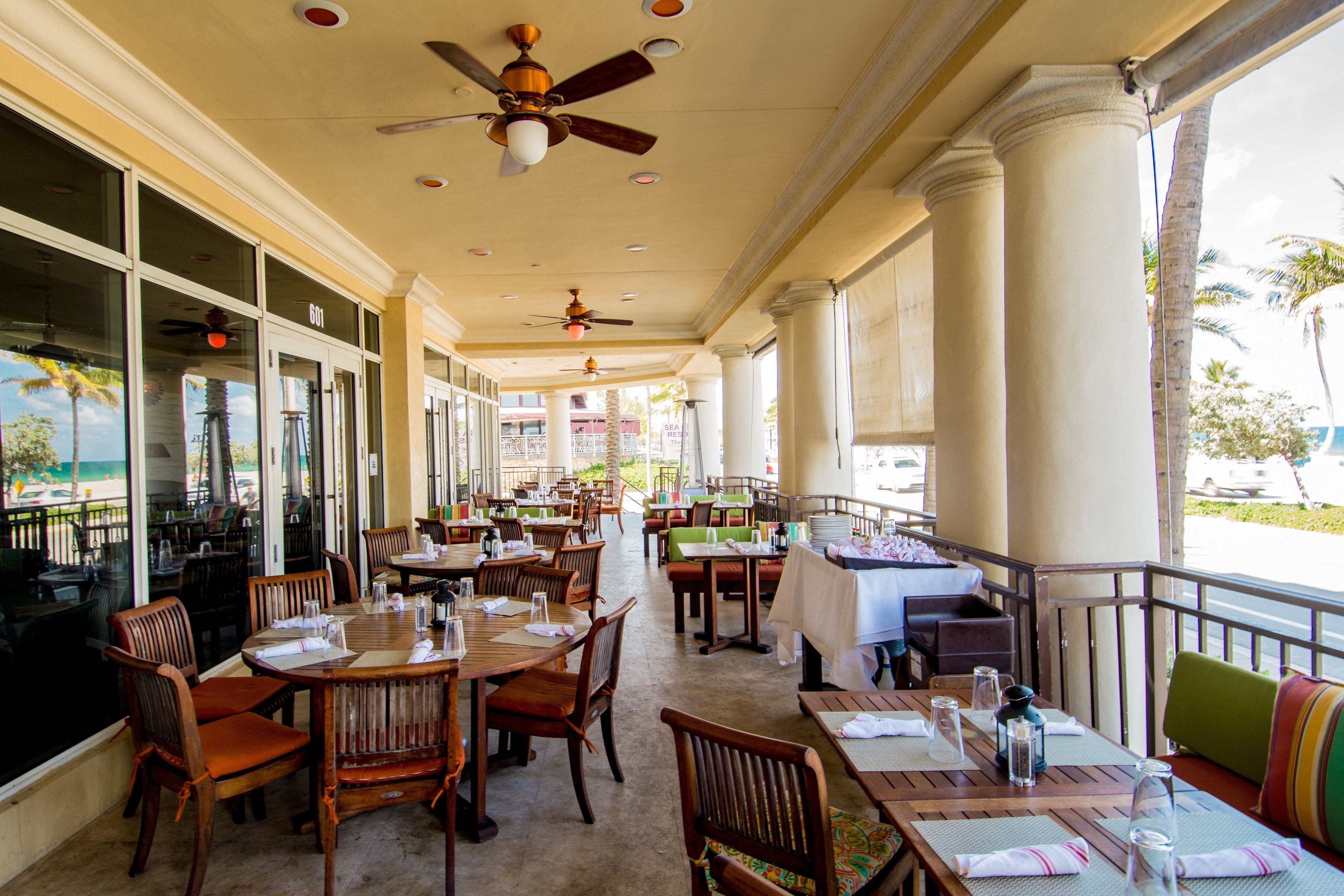 A restaurant with outdoor seating, wooden tables, and chairs, and a view of the ocean.