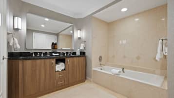 A modern bathroom with a wooden vanity, a large mirror, a bathtub, and beige tiled walls.