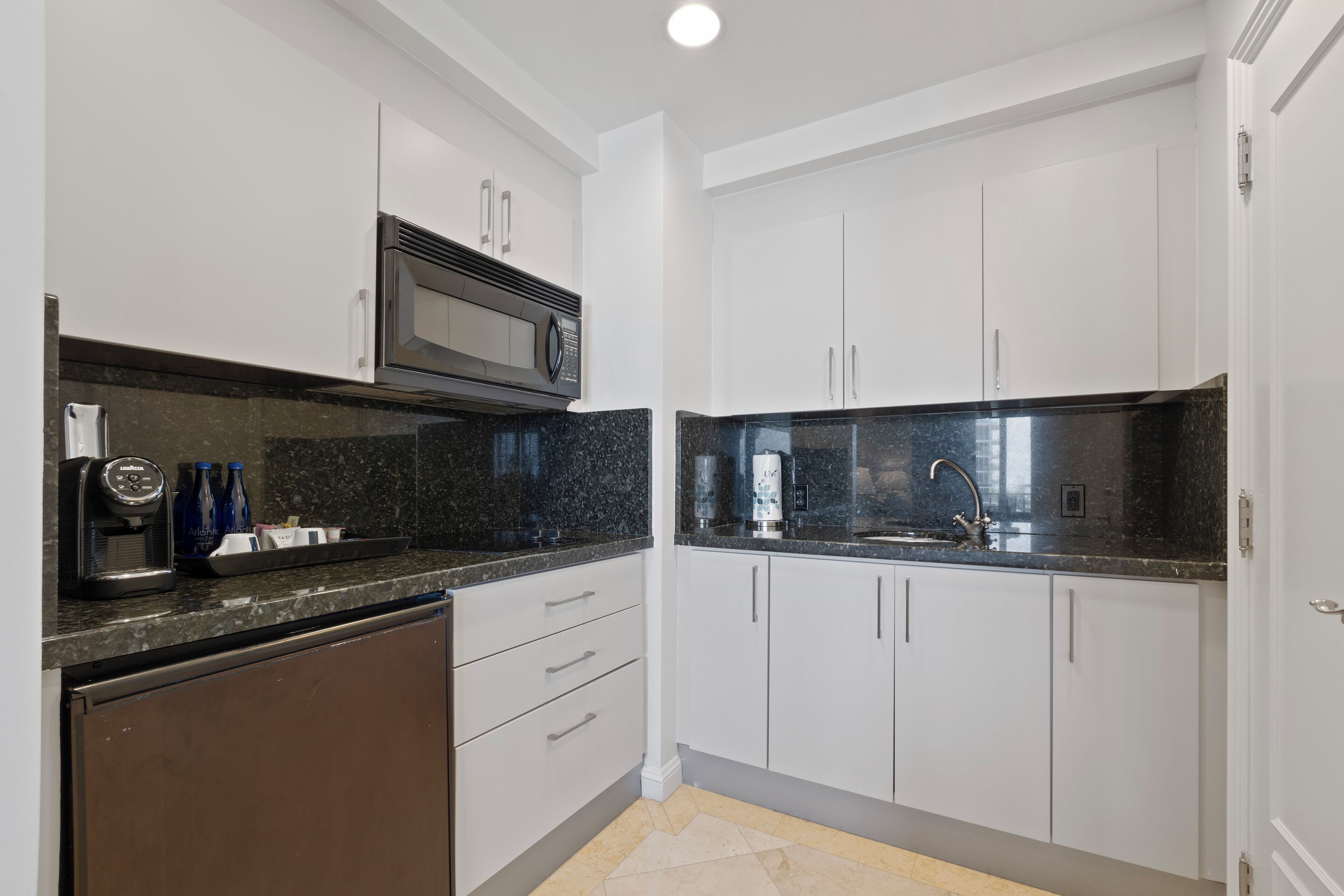 Una cocina moderna con armarios blancos, una encimera de granito negro y un microondas integrado.