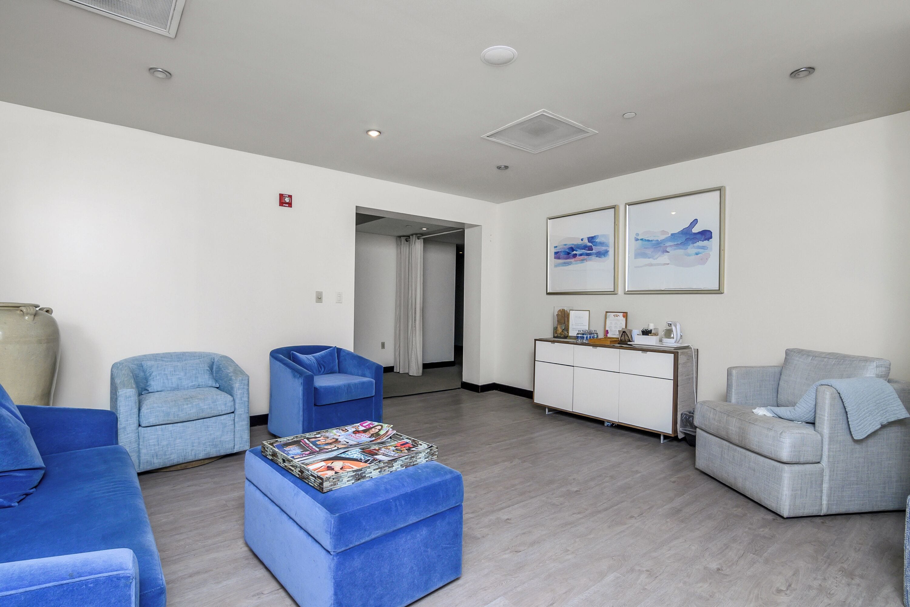 Ein moderner Lounge-Bereich mit blauen und grauen Sofas, einem weißen Schrank und zwei gerahmten Kunstwerken an der Wand.
