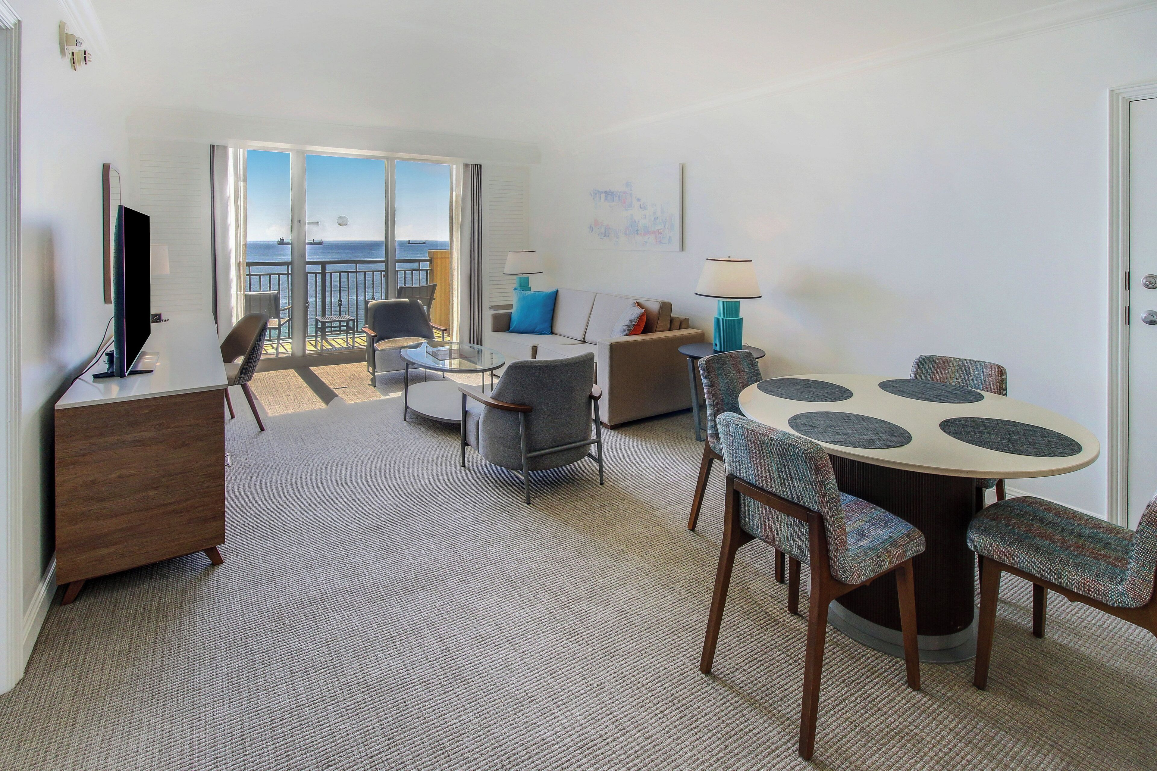 A hotel room with a balcony, a dining area with a round table, and a seating arrangement including a sofa and armchairs.