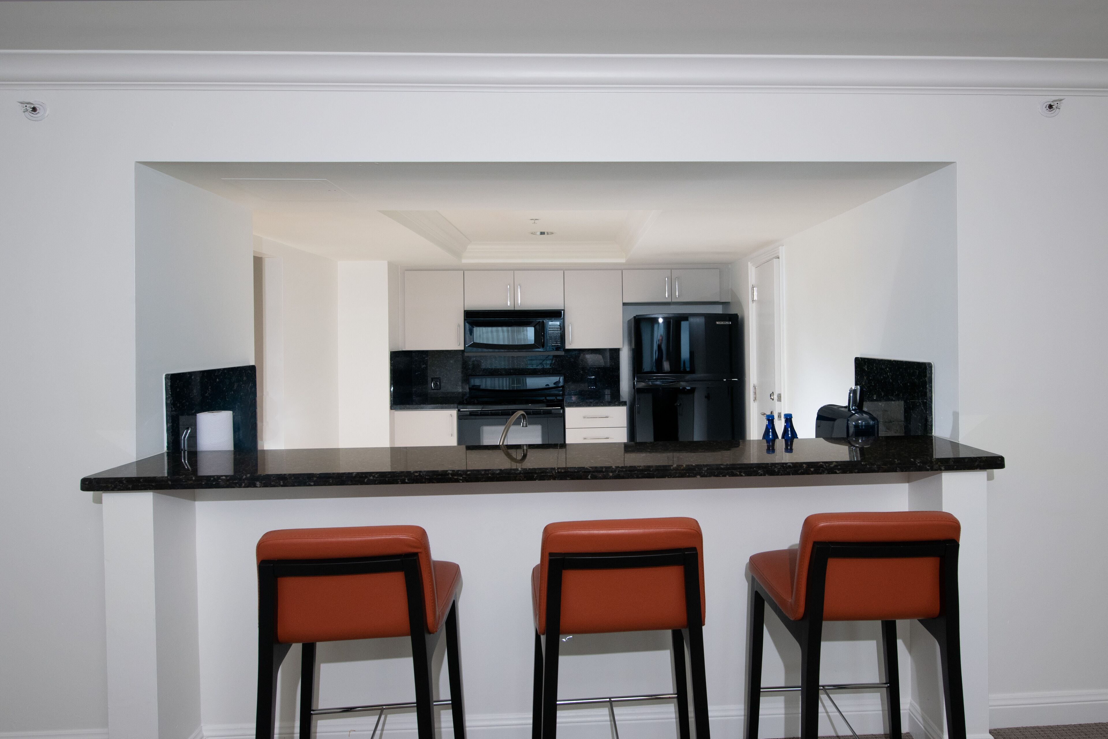 Une cuisine moderne dotée d’un îlot central, de trois tabourets de bar et d’un micro-ondes placé au-dessus de l’îlot.
