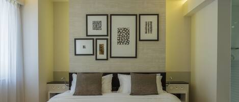 Una habitación de hotel moderna con una cama grande, una mesita de noche, un televisor montado en la pared y obras de arte enmarcadas.