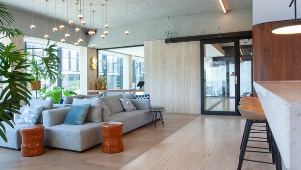 Un vestíbulo amplio con un sofá moderno, suelo de madera, lámparas colgantes y una zona de bar.