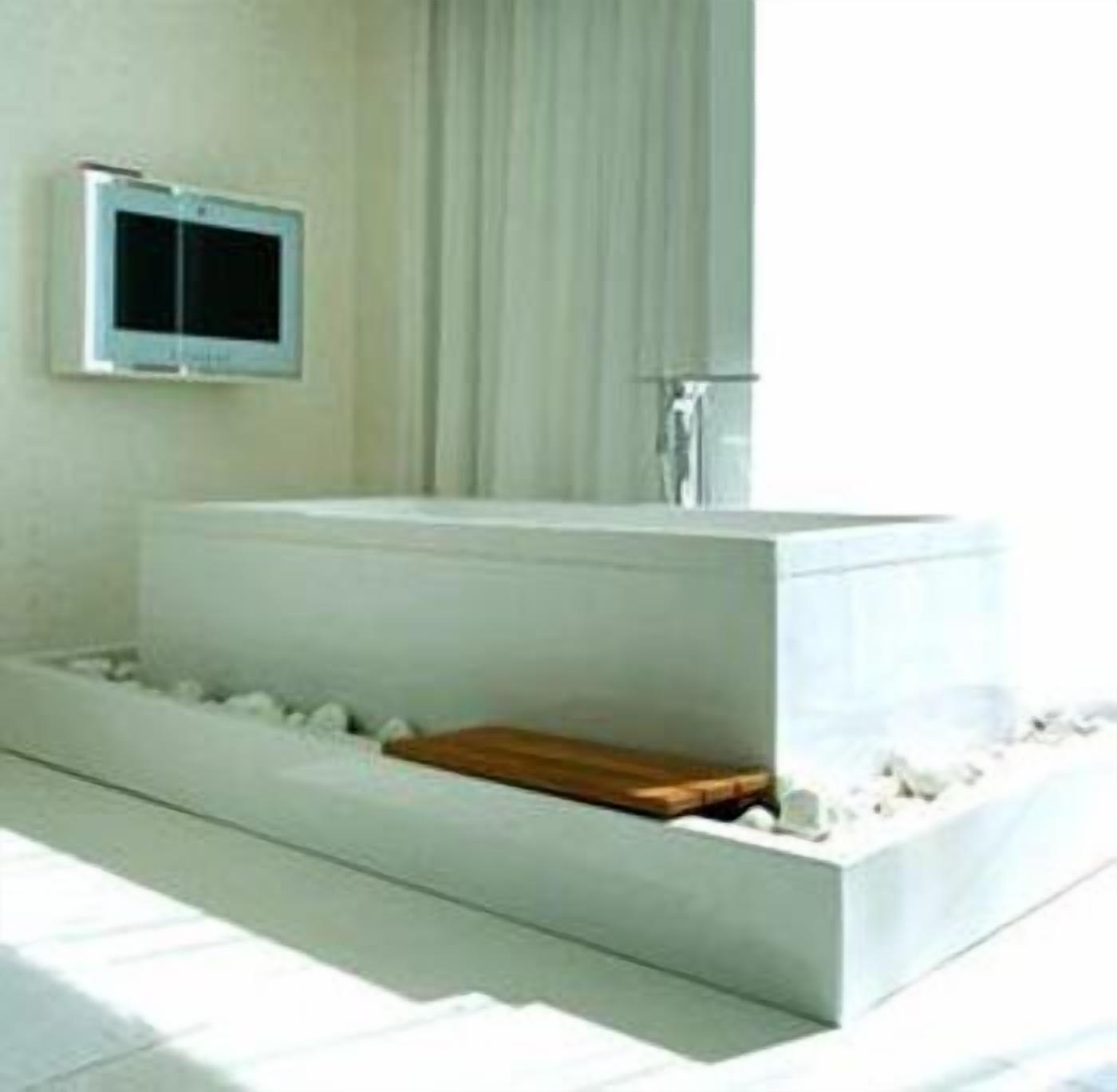 A modern bathroom with a large rectangular bathtub, a wooden bench, and a small television mounted on the wall.