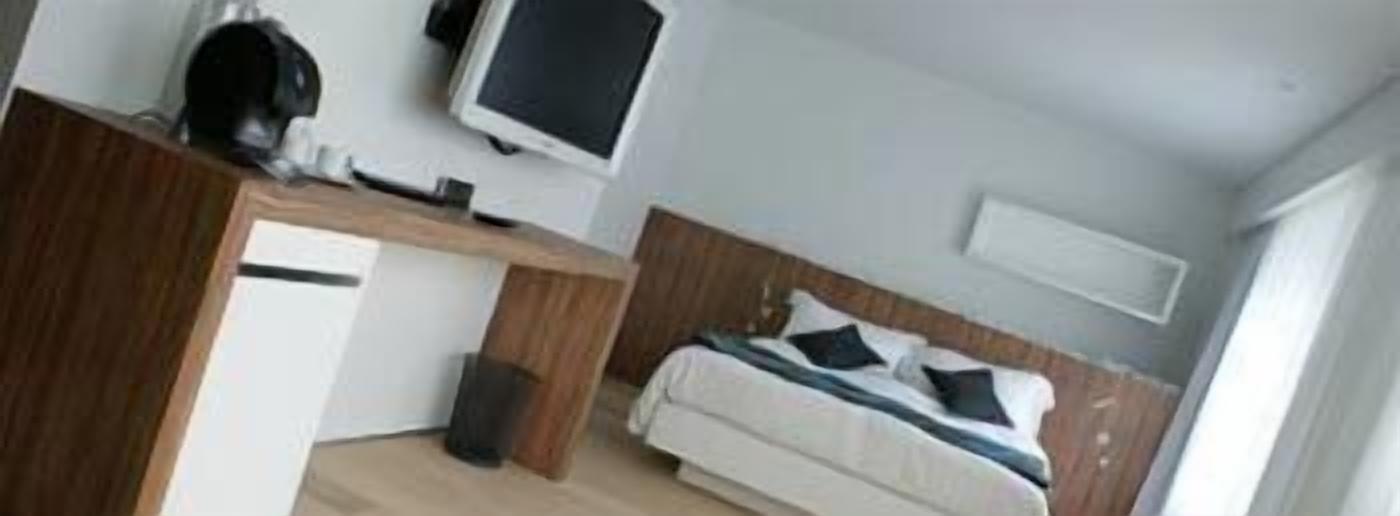 A bedroom with a bed, a desk, a chair, a television, and a small trash bin.