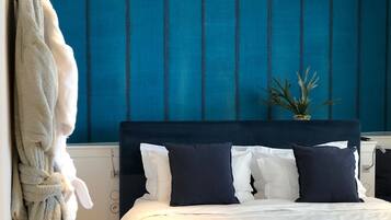 Habitación de hotel con una cama, ropa de cama blanca y azul oscuro, una pared azul y una planta en maceta.