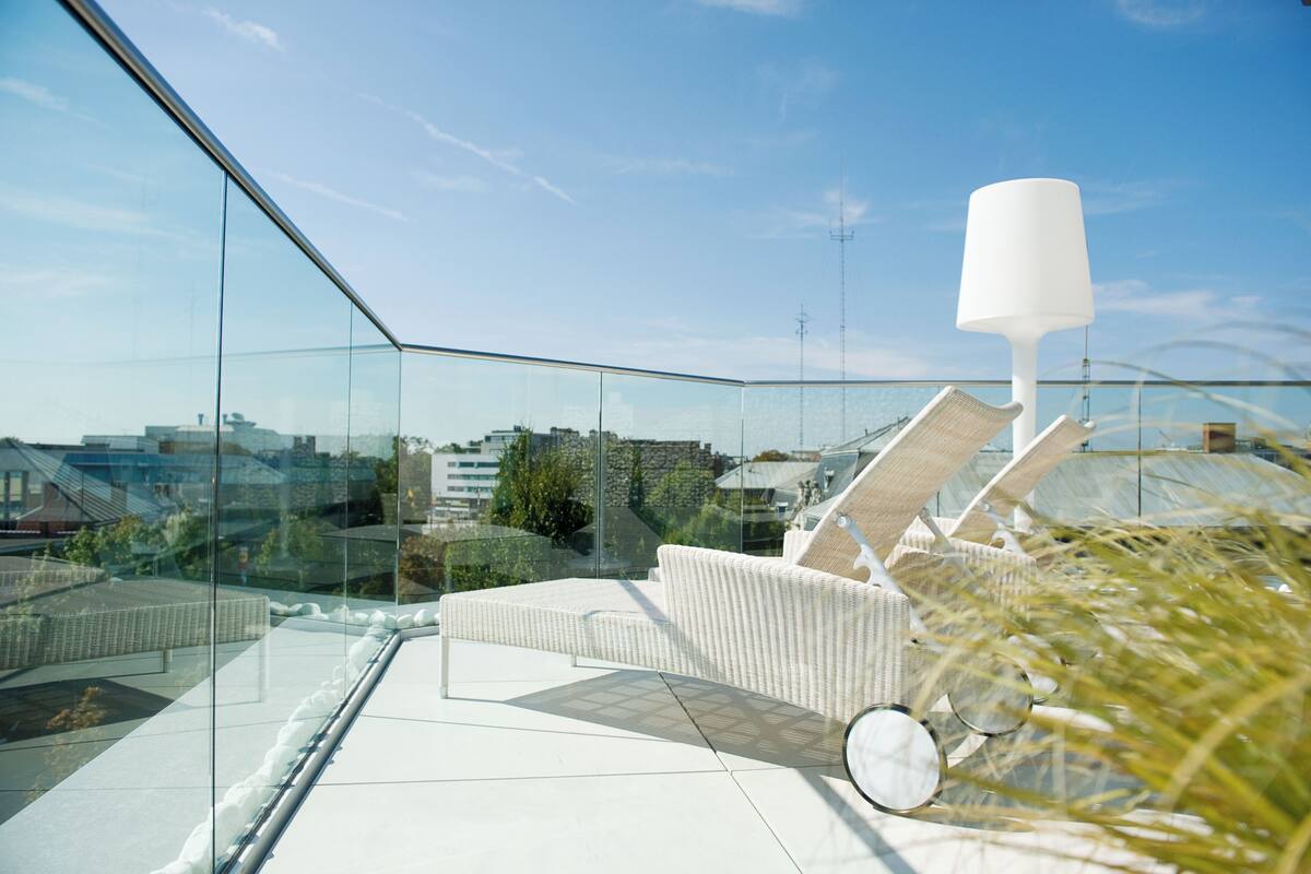 Een modern terras op het dak met glazen wanden, een witte lounge stoel en een witte lamp.