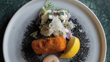 Un plato con una croqueta, ensalada y una cuña de limón sobre un plato con textura.