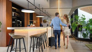 Un área de bar moderna con mostrador de madera, taburetes negros e iluminación colgante.
