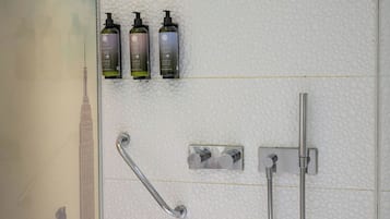 A bathroom with a handrail, a showerhead, and three bottles of shampoo on a textured wall.