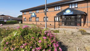 A Days Inn building with a brick facade, a signboard, and a parking area with flowers in the foreground. - Days Inn by Wyndham Warwick South M40 (Warwick)