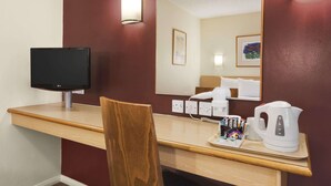 A hotel room with a wooden desk, a flat-screen TV, a white kettle, a coffee maker, and a mirror reflecting the room. - Days Inn by Wyndham Warwick South M40 (Warwick)
