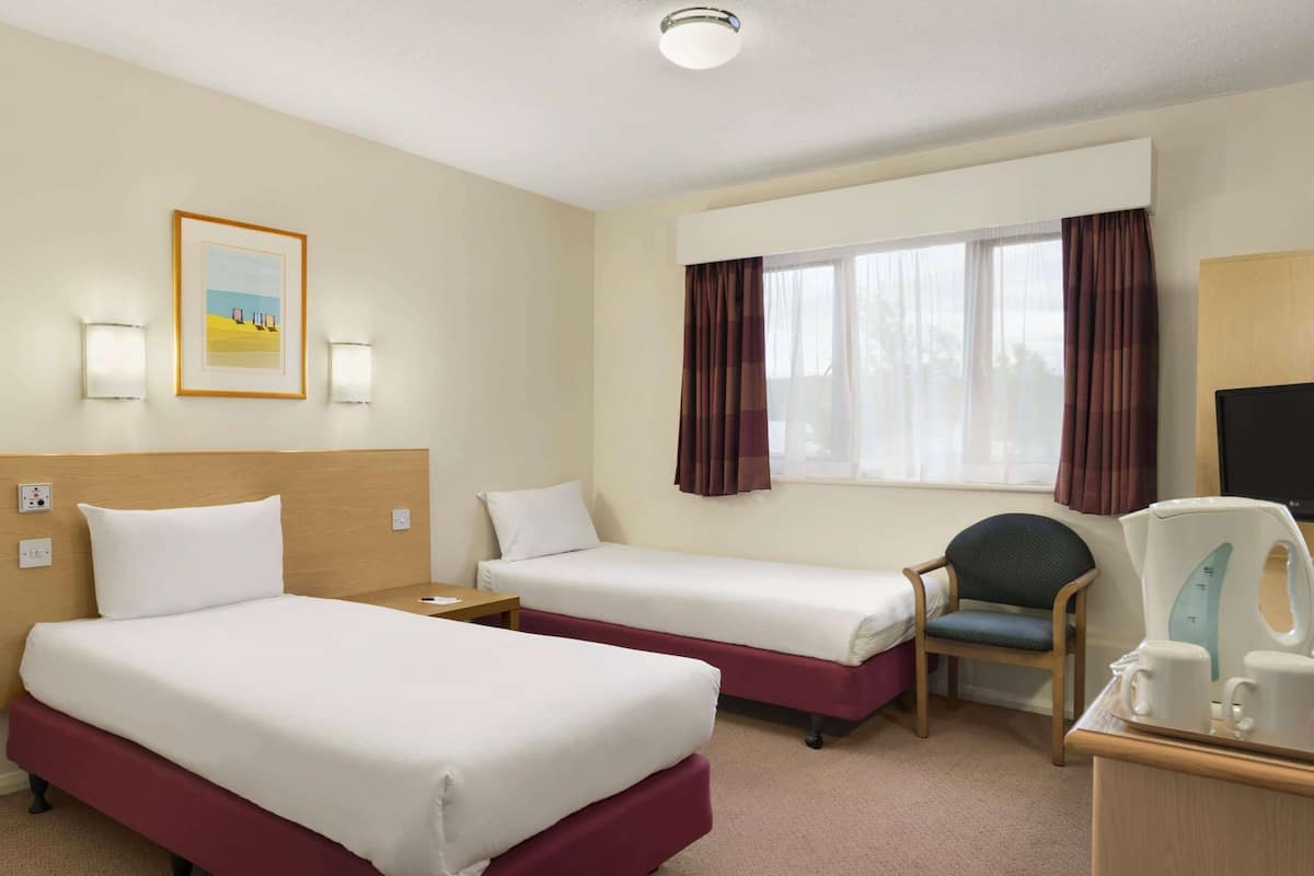 A hotel room with two beds, a desk, a chair, a window with curtains, and a painting on the wall.